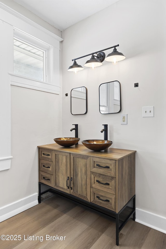 bathroom with baseboards, double vanity, a sink, and wood finished floors
