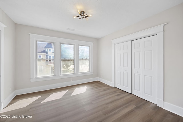 unfurnished bedroom with baseboards, dark wood finished floors, visible vents, a notable chandelier, and a closet