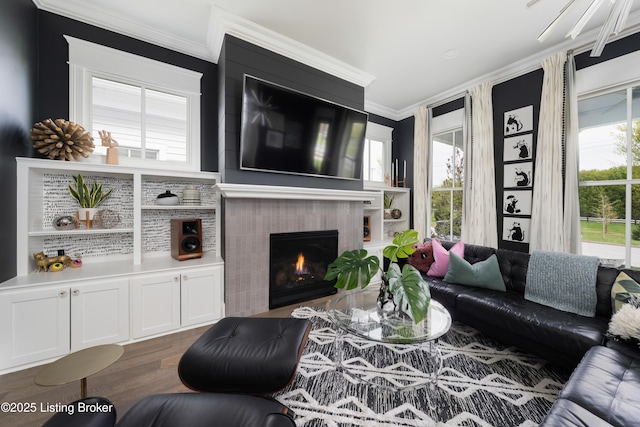 living area featuring wood finished floors, ornamental molding, and a warm lit fireplace