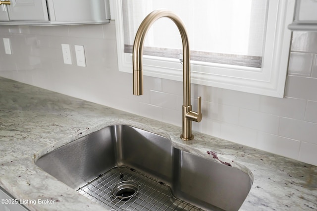 details featuring tasteful backsplash, light stone counters, a sink, and white cabinetry
