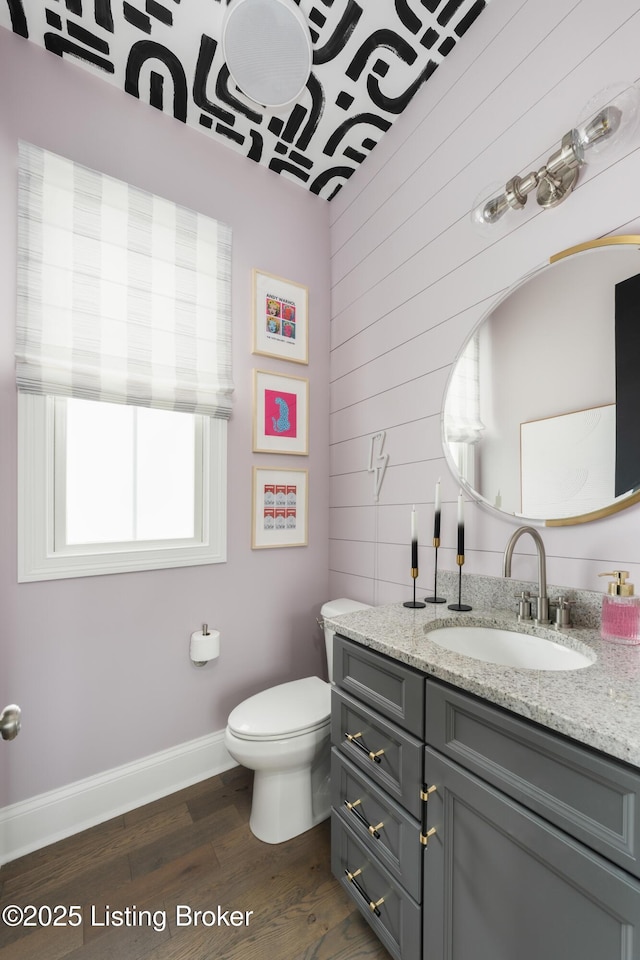 half bath with toilet, wood finished floors, vanity, and baseboards
