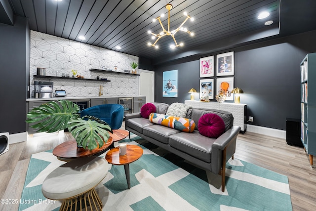 living area with baseboards, wooden ceiling, an accent wall, a dry bar, and a chandelier