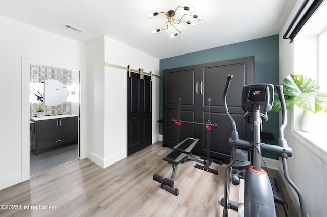 exercise room featuring visible vents, baseboards, a barn door, and light wood-style floors