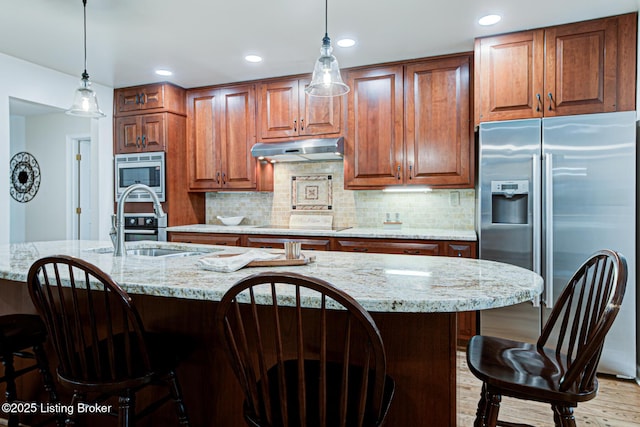 1014 Old Mill Stream Ln, Shepherdsville, KY 40165 - kitchen with appliances with stainless steel finishes, under cabinet range hood, a sink, light wood-style flooring, and a kitchen breakfast bar