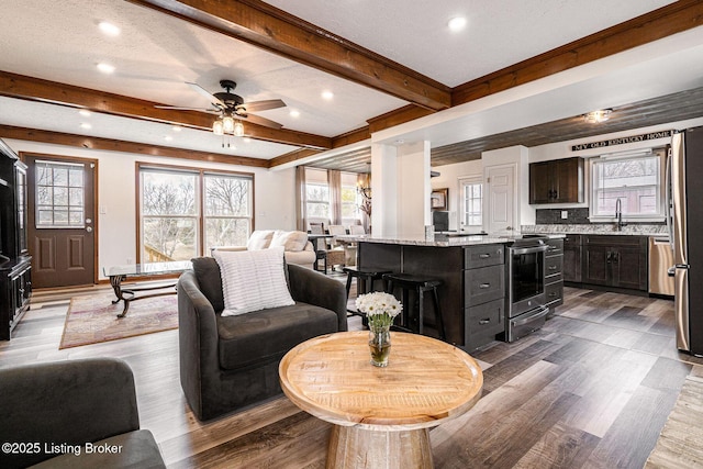 living area with plenty of natural light, a ceiling fan, beam ceiling, and wood finished floors