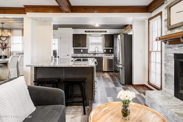 kitchen featuring dark brown cabinetry, light stone counters, beam ceiling, stainless steel appliances, and dark wood-type flooring