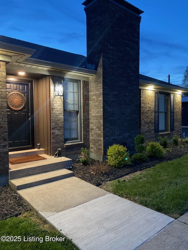 doorway to property featuring a chimney and brick siding