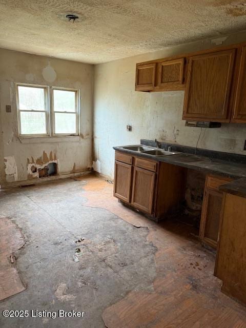 kitchen featuring a textured ceiling, a sink, dark countertops, and brown cabinetry