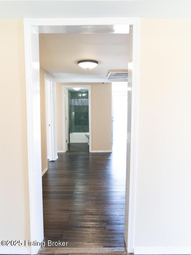 hallway featuring dark wood finished floors, baseboards, and visible vents
