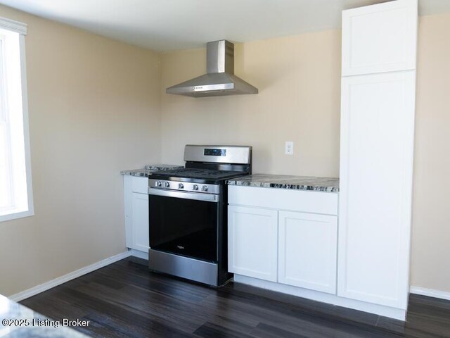 kitchen featuring stainless steel gas stove, dark wood finished floors, stone countertops, wall chimney range hood, and white cabinets