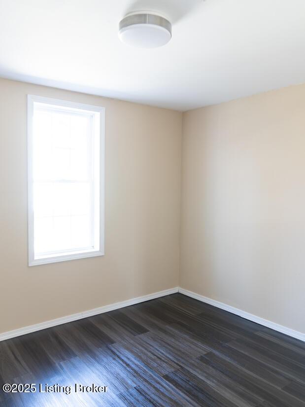 spare room with baseboards and dark wood-style flooring