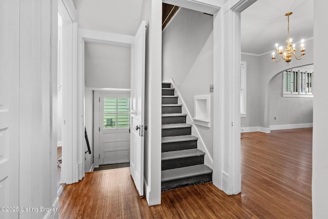 stairway with baseboards, ornamental molding, a chandelier, arched walkways, and wood finished floors