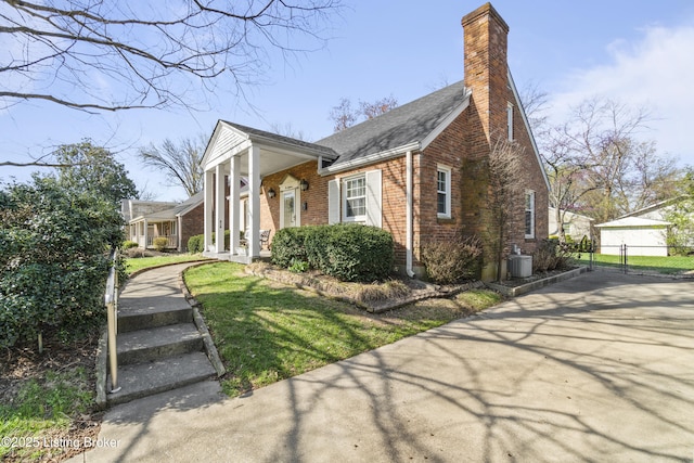 view of front facade with brick siding, a front lawn, a chimney, and central AC unit