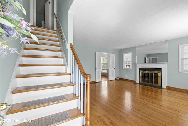 stairs featuring baseboards, a fireplace with flush hearth, wood finished floors, and a textured ceiling