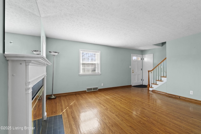 unfurnished living room featuring visible vents, a textured ceiling, wood finished floors, and a fireplace with flush hearth