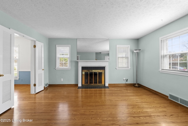 unfurnished living room with visible vents, wood finished floors, a fireplace with flush hearth, and a textured ceiling