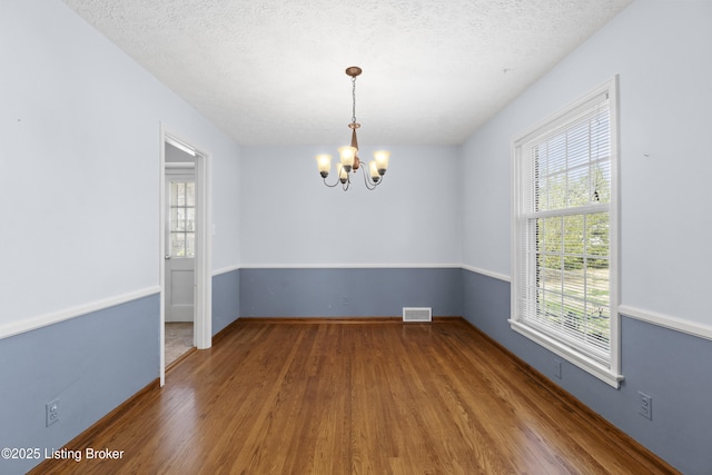 spare room featuring a chandelier, a wealth of natural light, visible vents, and wood finished floors