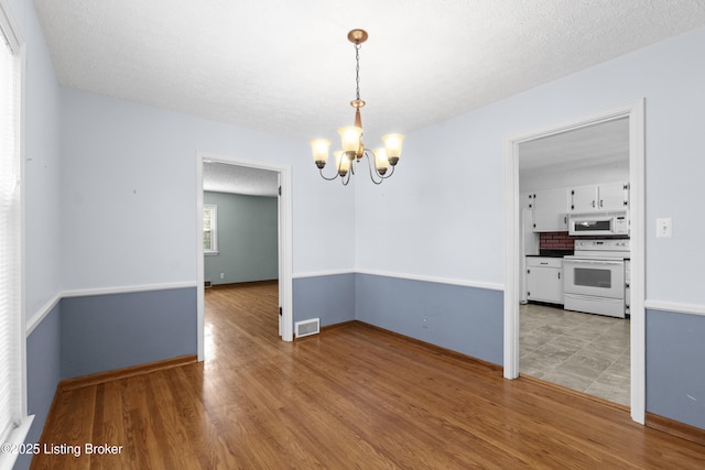 unfurnished dining area with light wood-style floors, an inviting chandelier, baseboards, and visible vents