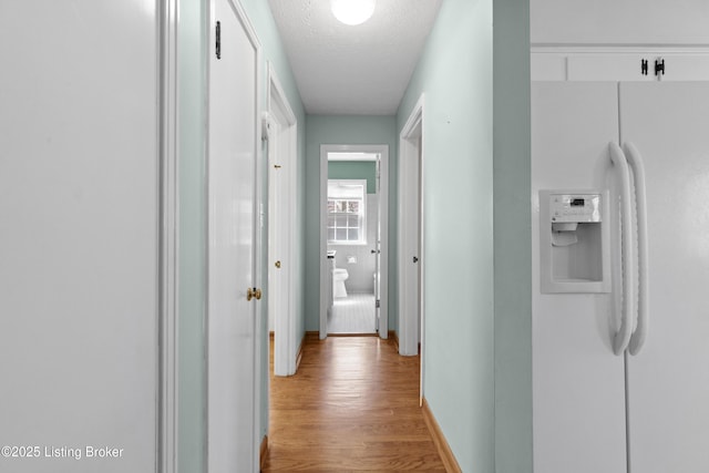 hall featuring light wood-style flooring, baseboards, and a textured ceiling