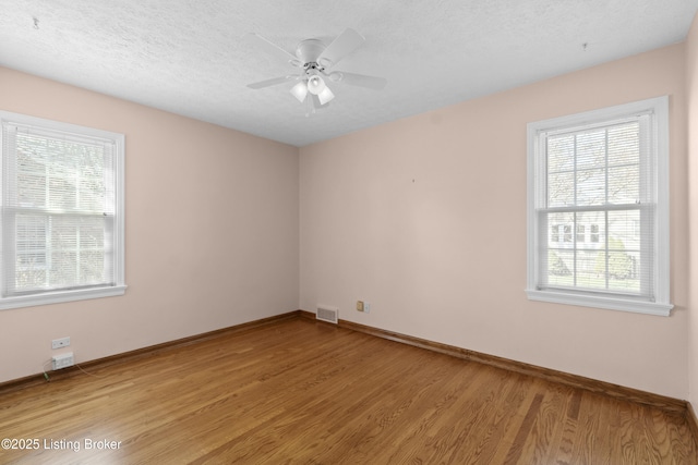 empty room with a wealth of natural light, light wood finished floors, visible vents, and baseboards