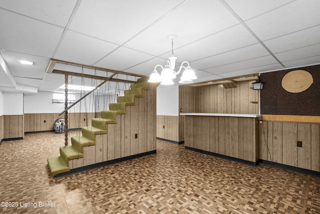 interior space with wainscoting, wooden walls, a drop ceiling, and stairs