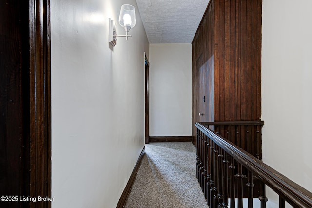 corridor featuring baseboards, carpet floors, and a textured ceiling