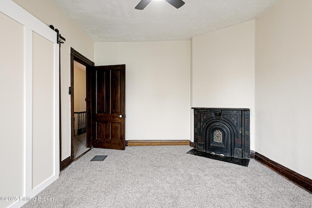 unfurnished living room with baseboards, carpet floors, a barn door, visible vents, and ceiling fan