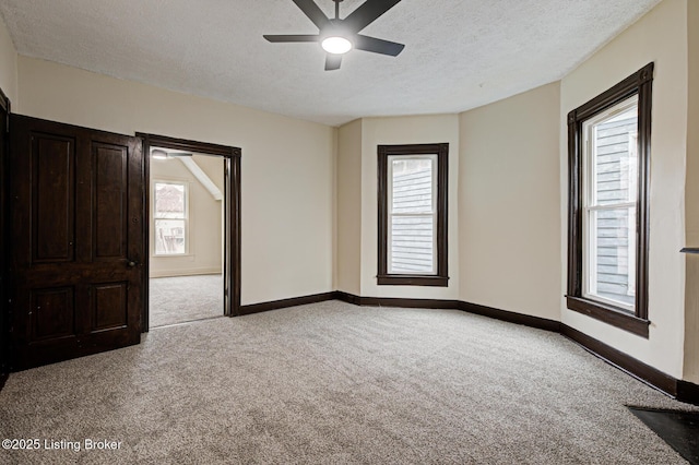 empty room featuring light carpet, a textured ceiling, baseboards, and a ceiling fan