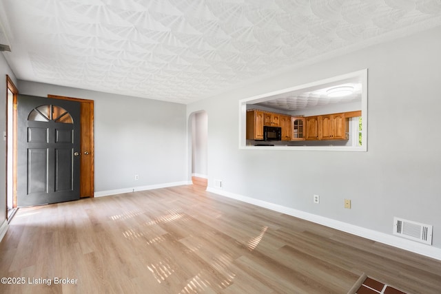 6515 Upper Hunters Trce, Louisville, KY 40216 - unfurnished living room featuring visible vents, arched walkways, baseboards, and light wood-type flooring