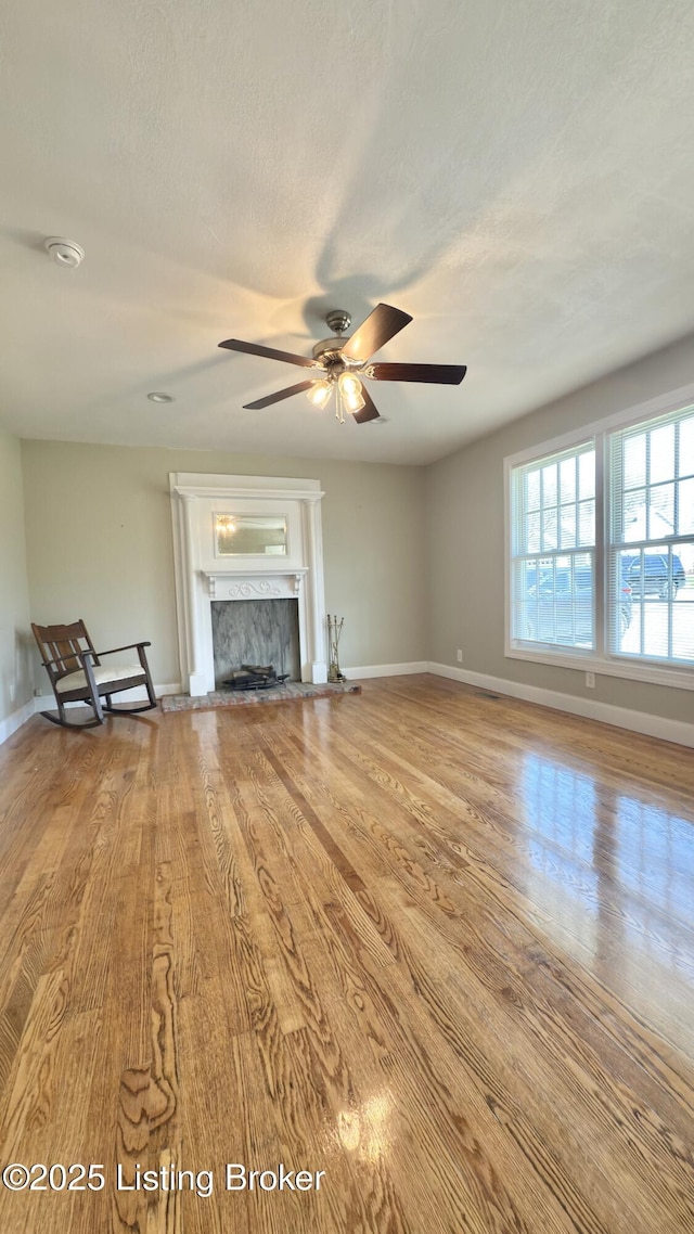 unfurnished living room featuring baseboards, a textured ceiling, ceiling fan, a high end fireplace, and wood finished floors