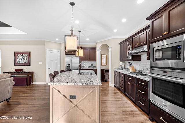 kitchen featuring open floor plan, ornate columns, stainless steel appliances, under cabinet range hood, and a sink