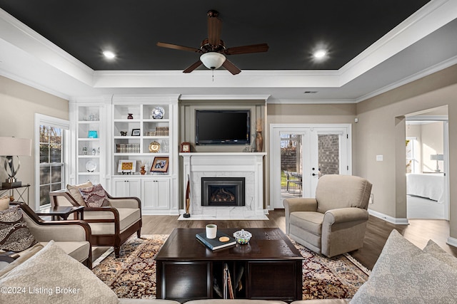 living room with a ceiling fan, a raised ceiling, a tiled fireplace, and wood finished floors