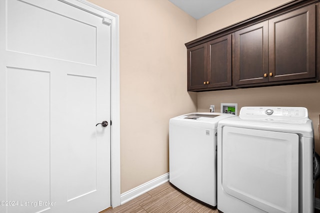 clothes washing area featuring baseboards, washing machine and clothes dryer, cabinet space, and light wood-style floors