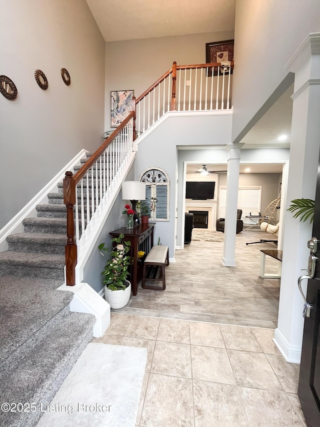 stairs featuring a fireplace, a high ceiling, baseboards, and decorative columns
