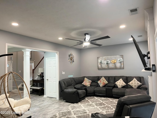 living room with stairway, light wood-type flooring, ceiling fan, visible vents, and ornate columns