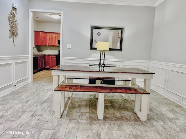 dining room featuring a decorative wall, crown molding, a wainscoted wall, and light wood-style floors