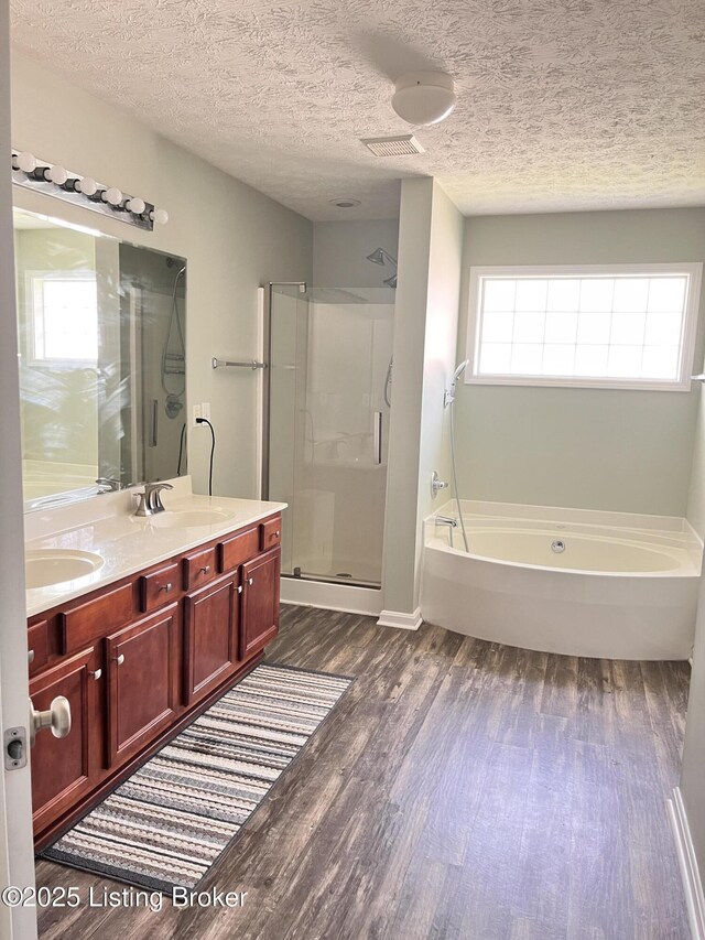 bathroom with a shower stall, wood finished floors, double vanity, a sink, and a garden tub