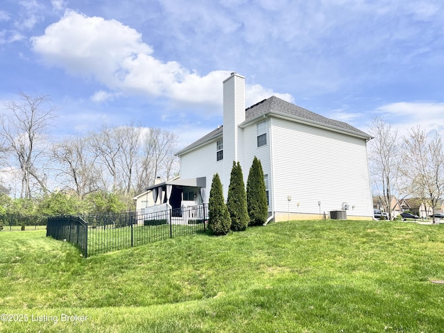 view of side of property with a chimney, fence, a yard, and central AC