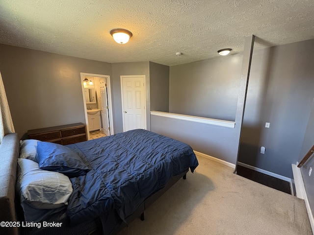 carpeted bedroom featuring ensuite bathroom, baseboards, and a textured ceiling