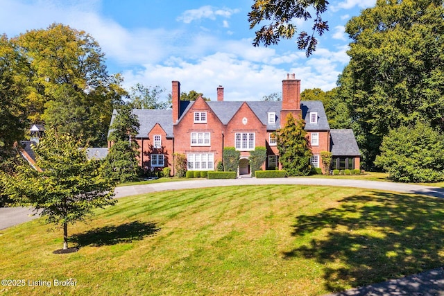 tudor house featuring a chimney, a front lawn, and curved driveway