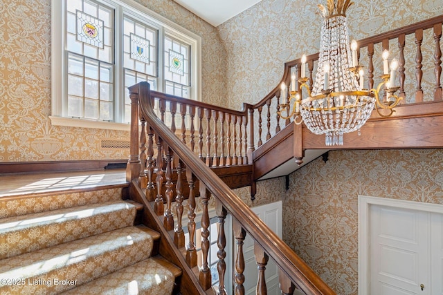 stairs with a chandelier and wallpapered walls