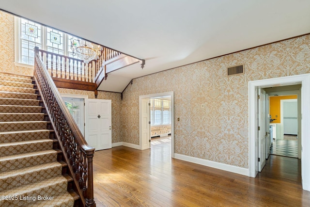 stairway with visible vents, an inviting chandelier, wood finished floors, and wallpapered walls