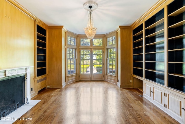 unfurnished living room with built in shelves, an inviting chandelier, crown molding, wood finished floors, and a premium fireplace