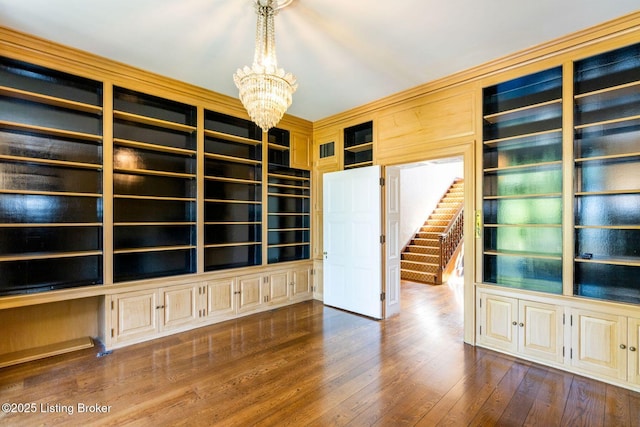 empty room with a chandelier, dark wood-type flooring, built in features, and stairway