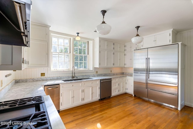 kitchen with light wood-type flooring, white cabinetry, stainless steel appliances, pendant lighting, and a sink
