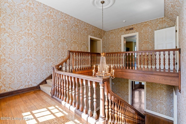 stairway featuring hardwood / wood-style floors, wallpapered walls, a notable chandelier, and visible vents
