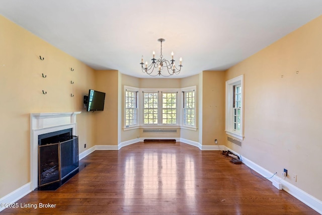 unfurnished living room with a fireplace with flush hearth, a notable chandelier, baseboards, and wood finished floors