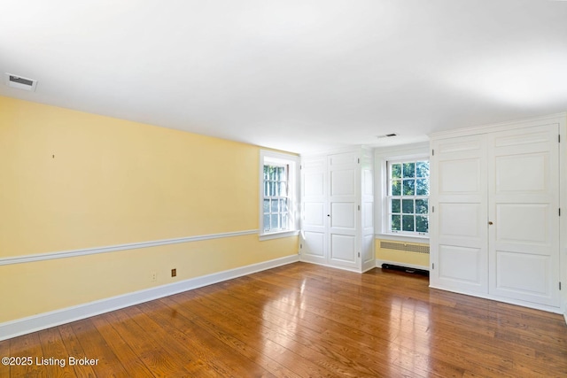 unfurnished room with visible vents, baseboards, radiator, and hardwood / wood-style flooring