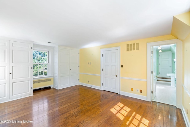 unfurnished bedroom with ensuite bathroom, radiator heating unit, visible vents, wood-type flooring, and baseboards