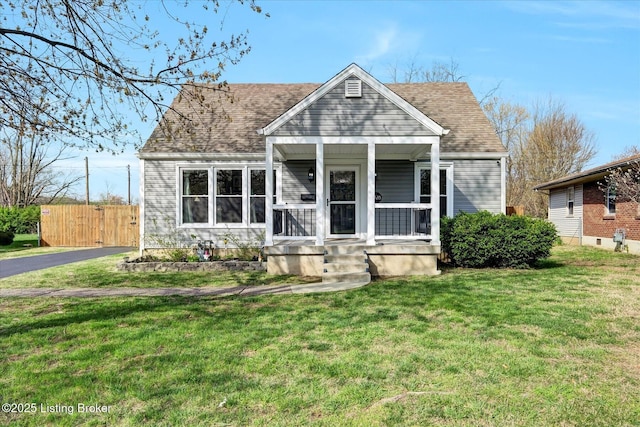 view of front of house with a shingled roof, fence, a front lawn, and covered porch